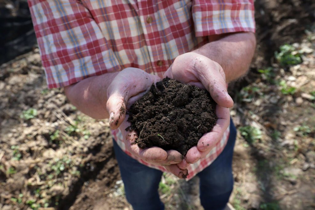Hands holding dark, rich soil that is healthy and forming aggregates from regenerative treatment through "the biotic climate."